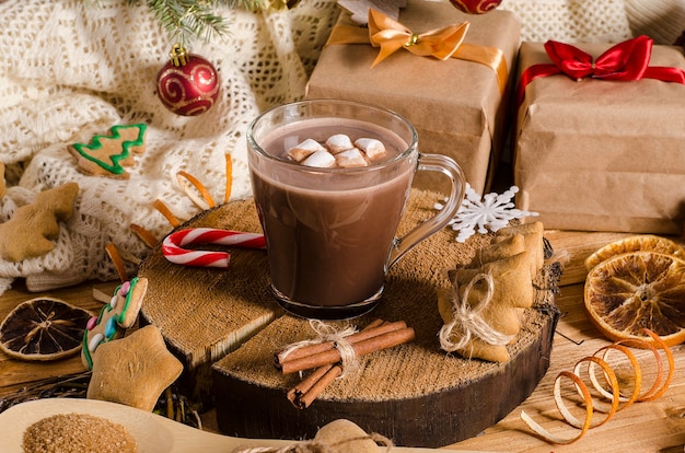 Bebida quente de cacau com marshmallows de Natal e ano novo em uma mesa com presentes, biscoitos de Natal e galhos de árvores de Natal. Chocolate quente.