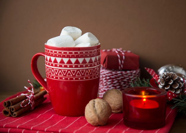 Bebida quente de Natal cacau e marshmallow no copo vermelho com presentes caixas cabo Sparkles nozes varas de canela pinhas cones vela abeto ramo de árvore em fundo escuro. Inverno