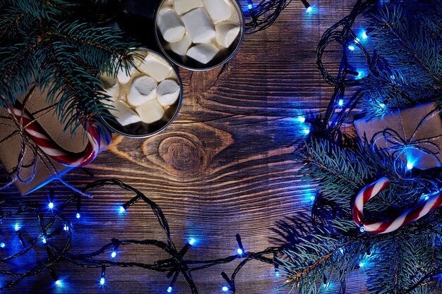 Bebida quente de Natal. Chocolate quente com marshmallow, caixa de presente, luzes de Natal, festão e ramos de abeto em um fundo de madeira. Vista do topo. Copie o espaço. Postura plana. Ainda vida. Brincar