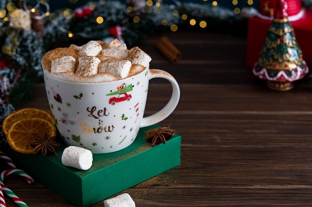 Bebida quente de Natal com marshmallows e especiarias em um fundo de ramos de pinheiro nevado. Fundo vintage festivo.