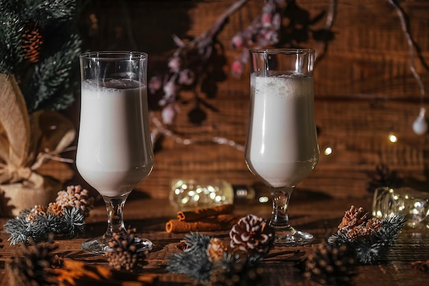 Bebida quente de Natal Eggnog com canela é derramada em dois copos sobre fundo de madeira