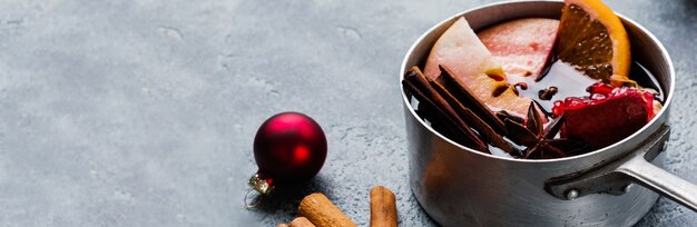 Bebida quente de vinho quente com frutas cítricas, maçã, romã e especiarias em caçarola de alumínio com brinquedos antigos para árvores de natal e galho de abeto em fundo de concreto. foco seletivo.