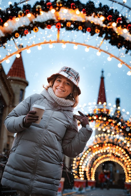 Foto bebida quente de xícara de menina enquanto caminhava no mercado de natal decorado com luzes de férias à noite ha