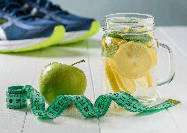 Una bebida recién preparada hecha de limón, menta y manzana sobre una mesa blanca y zapatillas deportivas.