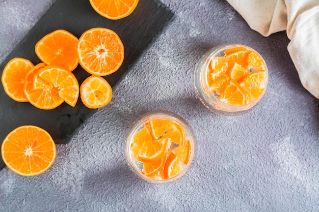 Bebida refrescante agua mineral con trozos de mandarina en vasos y frutas maduras al lado de la mesa. Comida de desintoxicación. Vista superior