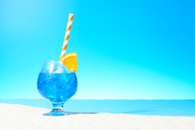 Foto bebida refrescante azul con hielo y una rodaja de naranja en un vaso en la costa arenosa