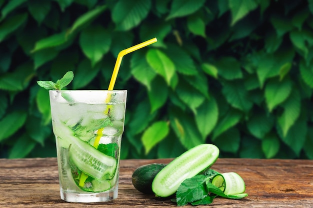 Bebida refrescante com pepino e hortelã em um copo com canudo ao lado de cubos de gelo contra um fundo verde