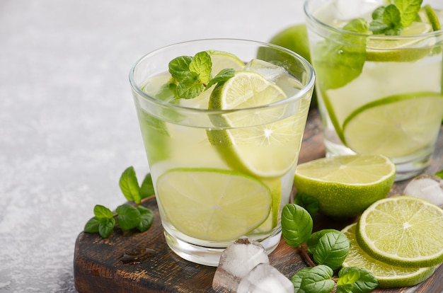 Bebida refrescante fría de verano con limón y menta en un vaso sobre concreto gris o piedra.