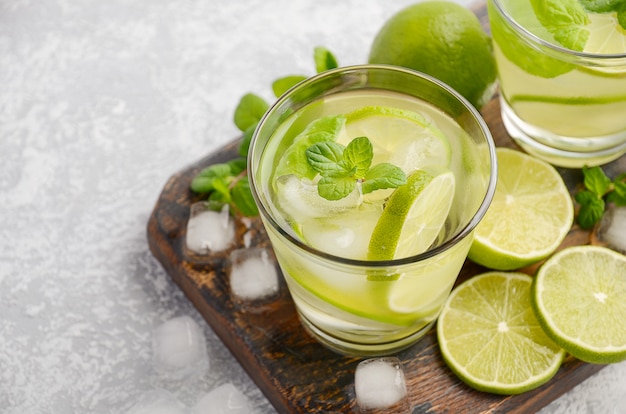 Bebida refrescante fría de verano con limón y menta en un vaso sobre concreto gris o piedra.