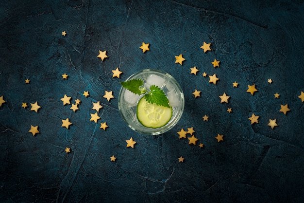 Bebida refrescante con hielo, pepino y menta sobre un fondo azul oscuro con estrellas. Concepto club nocturno, vida nocturna, fiesta, sed. Vista plana, vista superior