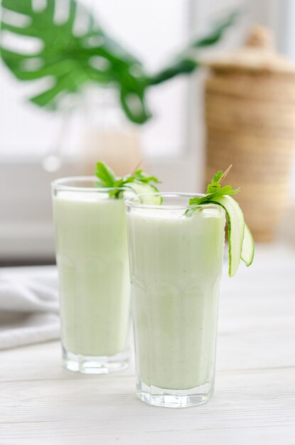 Bebida refrescante de leche fermentada con pepino y hierbas. Dos con un cóctel en un interior claro sobre una mesa blanca.