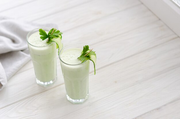 Bebida refrescante de leche fermentada con pepino y hierbas. Dos con un cóctel en un interior claro sobre una mesa blanca.