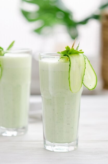 Bebida refrescante de leche fermentada con pepino y hierbas. dos con un cóctel en un interior claro sobre una mesa blanca.