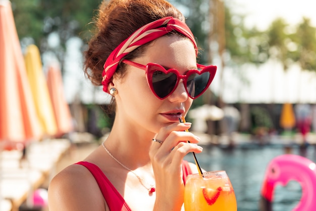 Bebida refrescante. Retrato de una joven y bella mujer sosteniendo una pajita mientras bebe su cóctel