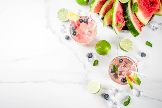 Bebida refrescante de verano, cóctel de limonada de sandía y arándanos con limón, menta y cubitos de hielo, fondo de mármol blanco