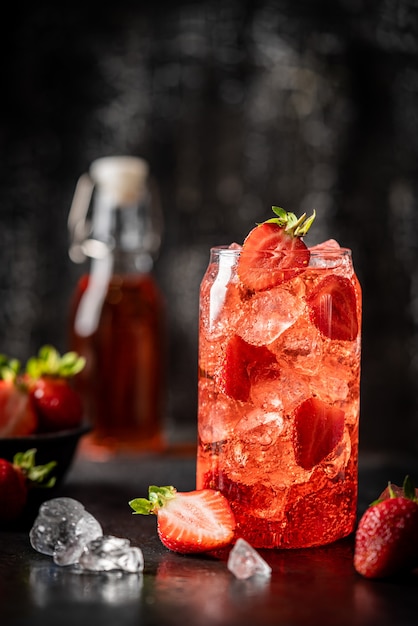 Bebida refrescante de verano con fresa y hielo en un vaso sobre fondo oscuro
