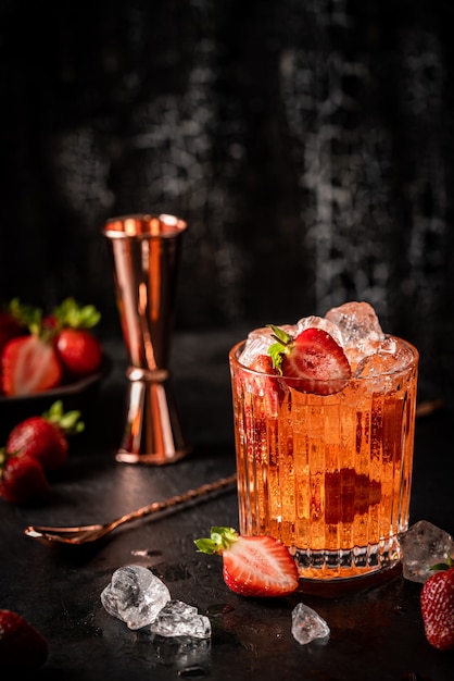 Bebida refrescante de verano con fresa y hielo en un vaso sobre fondo oscuro