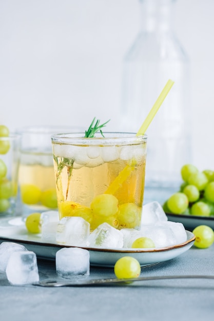 Bebida refrescante de verano en vaso con cubitos de hielo, uva verde y Romero sobre la mesa.