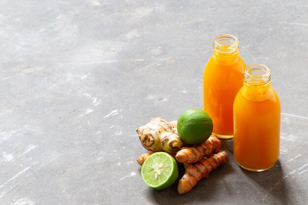 Bebida saludable de cúrcuma y raíces de jengibre y cal en pequeñas botellas en muro de hormigón gris con copyspace.