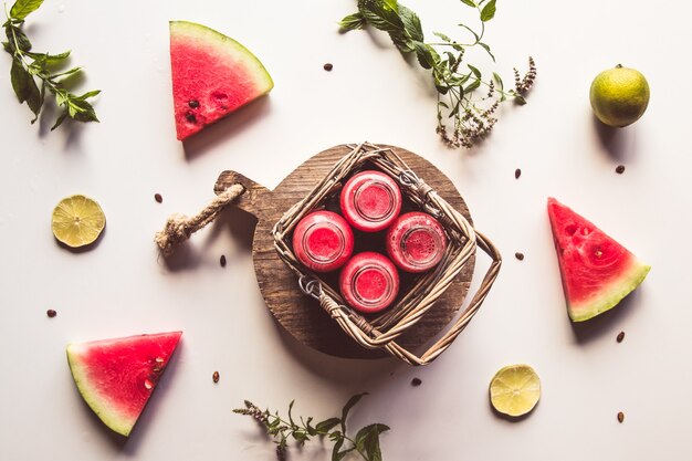 Bebida de sandía embotellada de verano sabroso en una cesta y rodajas de frutas frescas en blanco