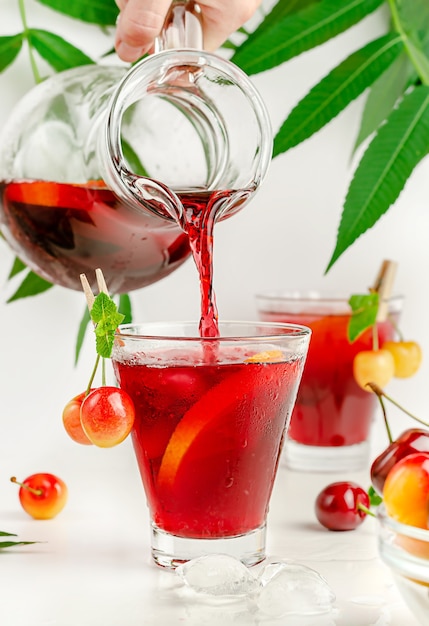 Bebida de sangría que se vierte de la jarra en el vaso sobre fondo blanco. Bebida refrescante de verano.