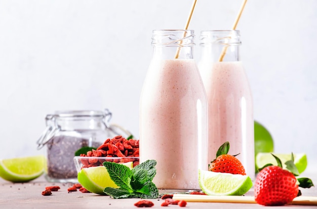 Bebida de superalimento mezclada saludable Batido de dieta orgánica con semillas de chía de fresa y bayas de goji y lima Botellas de vidrio con pajitas eco fendley Fondo gris con espacio de copia