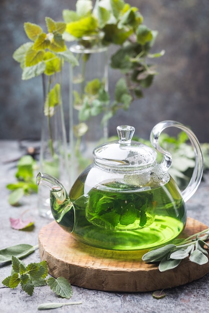 Bebida de té de menta sedante herbal caliente en una tetera de vidrio en una bandeja de madera con menta fresca del jardín