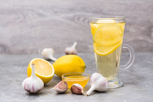 Bebida terapéutica de limón, miel y ajo en un vaso sobre la mesa. Medicina alternativa, tratamiento con remedios caseros.