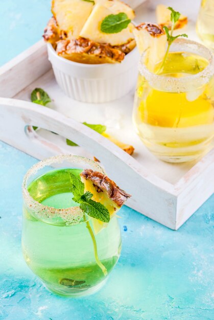 Foto bebida tropical margarita de suco de abacaxi coquetel com bandeja de madeira de fundo azul claro de hortelã fresca