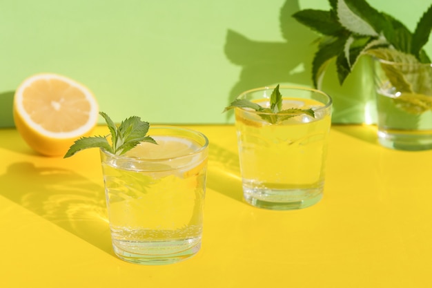 Bebida de verano. Bebida refrescante fresca con menta y limón en vaso. minimalismo. Limonada fresca natural con sombras duras sobre fondo amarillo