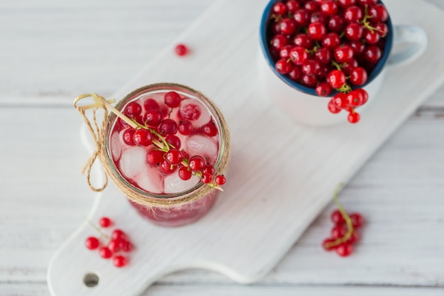 Bebida de verano con vino espumoso blanco. Cóctel de frutas refrescante casero o ponche con champán, grosellas rojas y cubitos de hielo sobre una madera blanca.