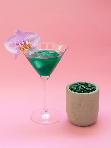 Foto bebida verde de espirulina líquida con phalaenopsis en copa de cóctel y pastillas de espirulina