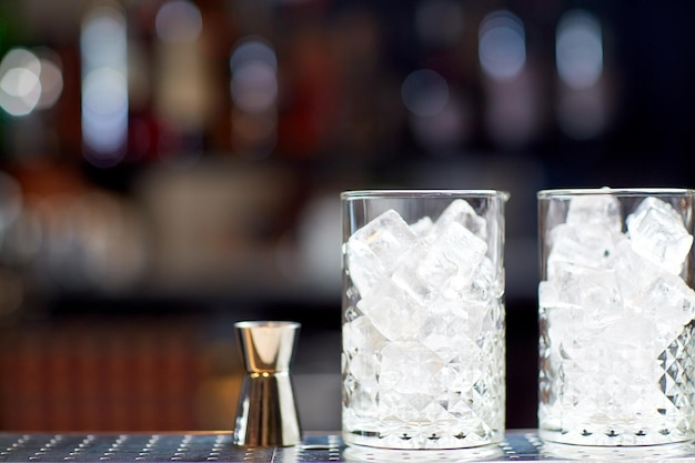 Foto bebidas alcohólicas y concepto de lujo: dos vasos antiguos con cubitos de hielo y jigger en la barra del bar