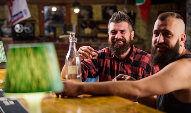 Foto bebidas alcohólicas fuertes amigos relajándose en el pub adicción al alcohol hombres borrachos relajándose en el pub divirtiéndose hipster brutal hombre bebiendo alcohol con un amigo en el mostrador del bar hombres bebiendo alcohol juntos