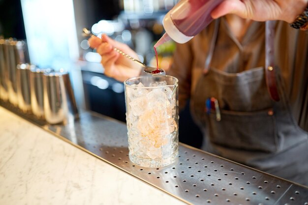 bebidas alcoólicas, pessoas e conceito de luxo - barman com vidro derramando xarope para mexer e preparar coquetel no balcão do bar