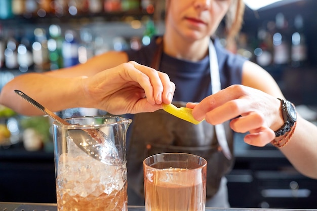 Foto bebidas alcoólicas, pessoas e conceito de luxo - barman mulher com copo e jarro preparando coquetel no bar