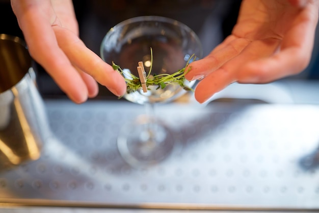 bebidas alcoólicas, pessoas e conceito de luxo - mãos de barman decorando vidro e preparando coquetel no bar