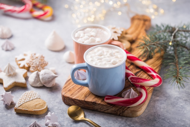 Bebidas de chocolate caliente de cacao con malvaviscos en tazas de color de Navidad en superficie gris. Bebida caliente tradicional, cóctel festivo en Navidad o Año Nuevo