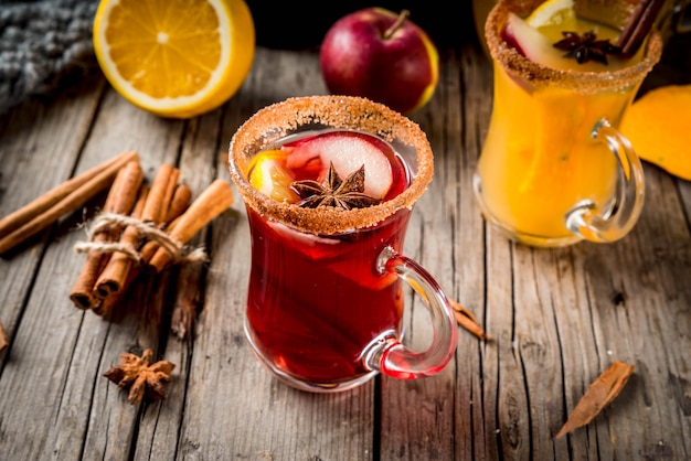 Bebidas y cócteles tradicionales de otoño e invierno. Blanco y rojo otoño sangría picante caliente con anís, canela, manzana, naranja, vino. En tazas de vidrio, antigua mesa de madera rústica. Enfoque selectivo copia espacio