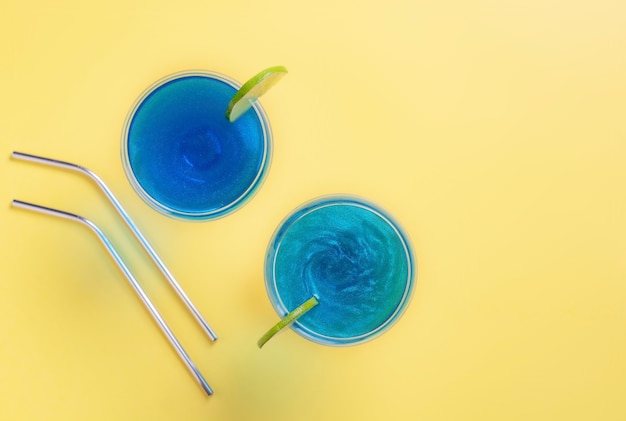 Bebidas com glitter azul espumante em copos de coquetel decorados com suporte de limão em um amarelo