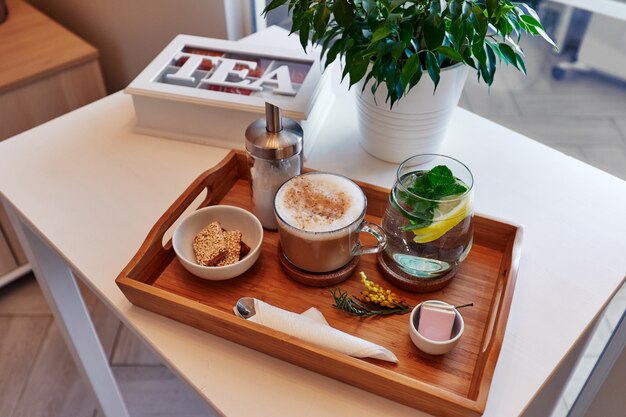 bebidas y comida en una bandeja de madera, café y limonada con dulces, una caja de té