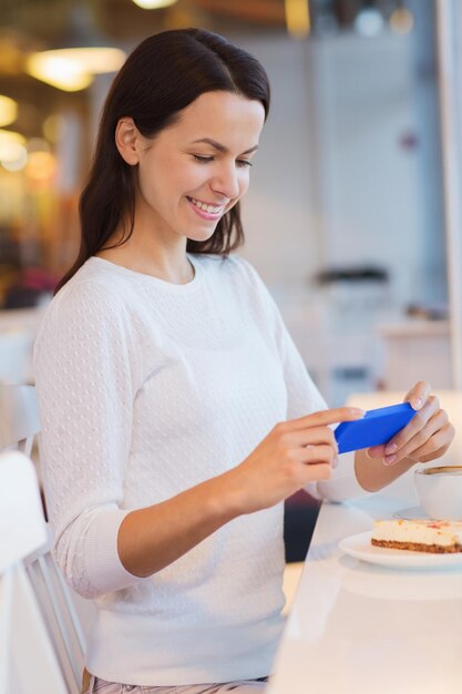 bebidas, comida, gente, tecnología y concepto de estilo de vida - joven sonriente tomando fotos con un smartphone y tomando café en la cafetería