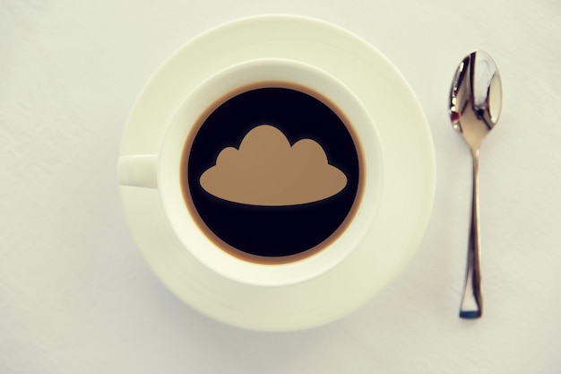 bebidas y concepto de tecnología de módem: taza de café negro con silueta de nube en la superficie, cuchara y platillo en la mesa