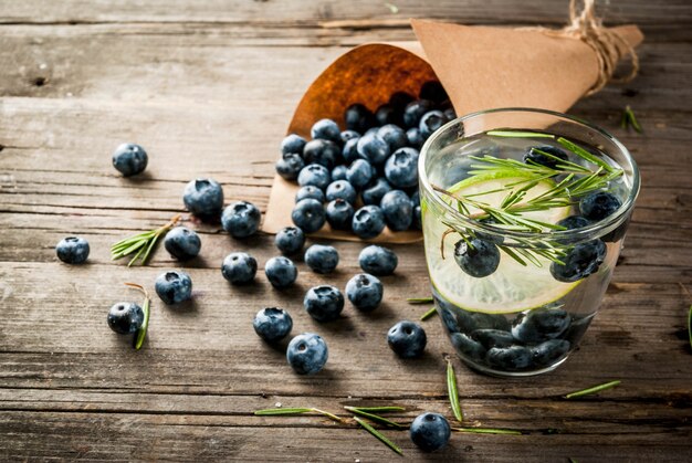 Bebidas de dieta de refresco de verão. Água de desintoxicação com infusão de alecrim, limão e mirtilos. Mesa de madeira rústica antiga copyspace