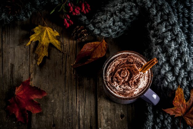 Bebidas de outono, chocolate quente ou cacau com chantilly e especiarias (canela, anis), na velha mesa de madeira rústica, com um cobertor quente e aconchegante, feno e folhas copiam espaço vista superior