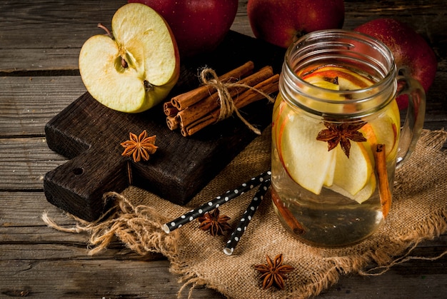 Bebidas de outono e inverno. Água de desintoxicação de outono com maçã, canela e pêra em frasco de vidro. Sobre uma madeira velha rústica, com ingredientes.