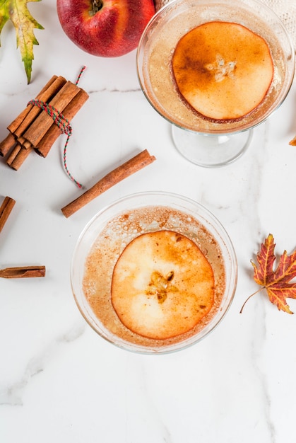 Bebidas de outono e inverno, margarida de martini de cidra de maçã com enfeite de maçã e canela, na mesa de mármore branca,