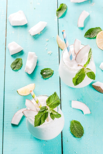 Bebidas de verão, coquetéis. Mojito de coco congelado com limão e hortelã. Piña colada. Em uma mesa de madeira verde azul clara com ingredientes. Copie o espaço