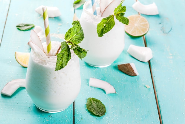 Foto bebidas de verão, coquetéis. mojito de coco congelado com limão e hortelã. piña colada. em uma mesa de madeira verde azul clara com ingredientes. copyspace