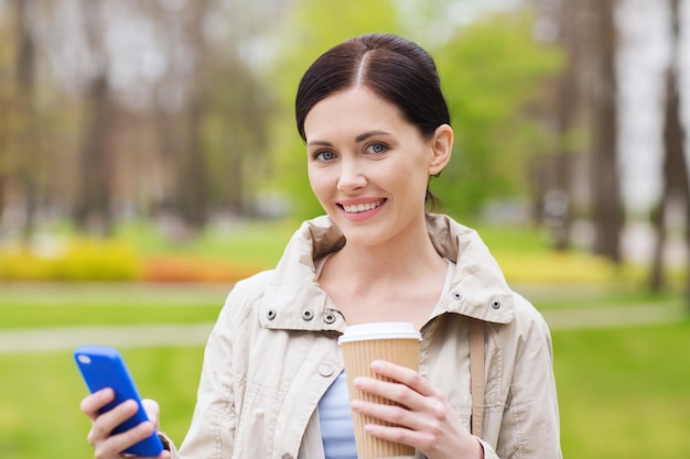 Bebidas, lazer, tecnologia e conceito de pessoas - mulher sorridente com smartphone e café no parque